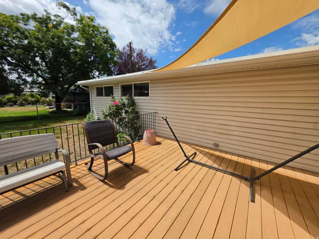 Expansive wood-finish deck with a black metal railing, vinyl siding, and multiple windows