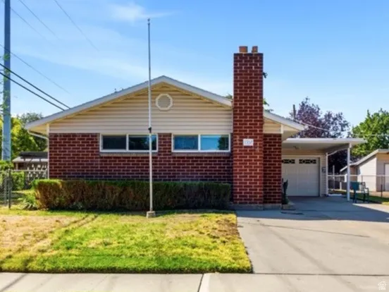 Brick and siding exterior featuring a prominent chimney, an attached carport, and an extended concrete driveway