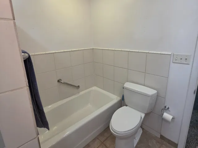 Recessed ceiling lighting, white ceramic wall tile, built-in bathtub, grab bar, and floor tile