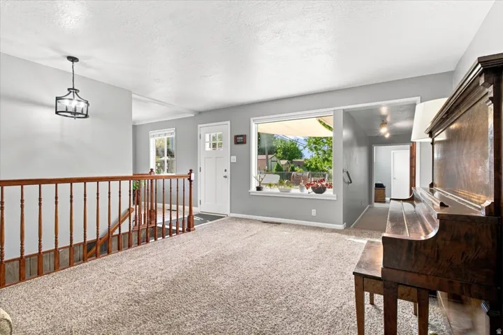 Carpeted flooring, contemporary chandelier, wood railing, large window, and white paneled door