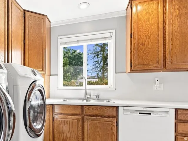 Light oak wood cabinetry, white countertops, stainless steel sink with a chrome faucet, white dishwasher, and tiled flooring