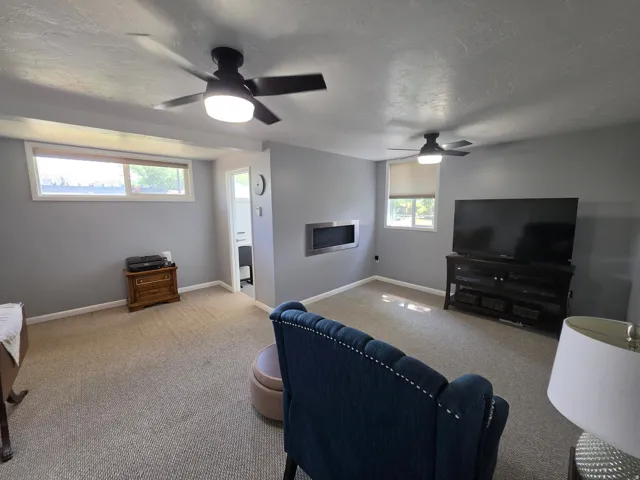 Recessed wall fireplace, two ceiling fans with integrated lighting, wall-to-wall carpeting, and multiple windows providing natural light
