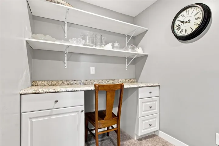 Built-in desk area featuring a light-toned countertop, white cabinetry with silver-toned hardware, and open white shelving