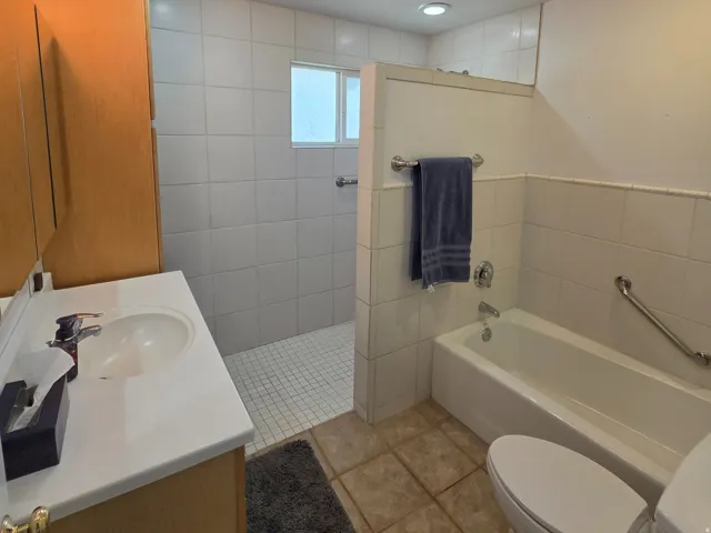 Bathroom featuring a built-in vanity with a white countertop, recessed lighting, a walk-in shower with white tile, a bathtub, and a window