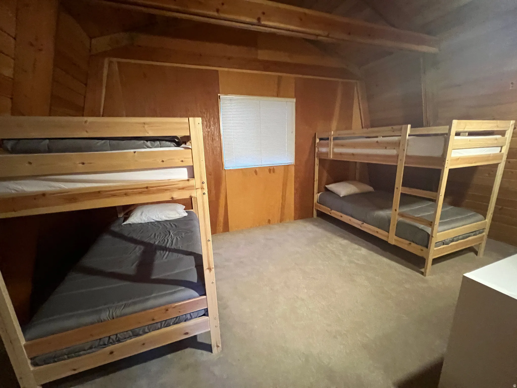 Wood-paneled room featuring two built-in bunk beds, neutral carpet flooring, and a single window with blinds