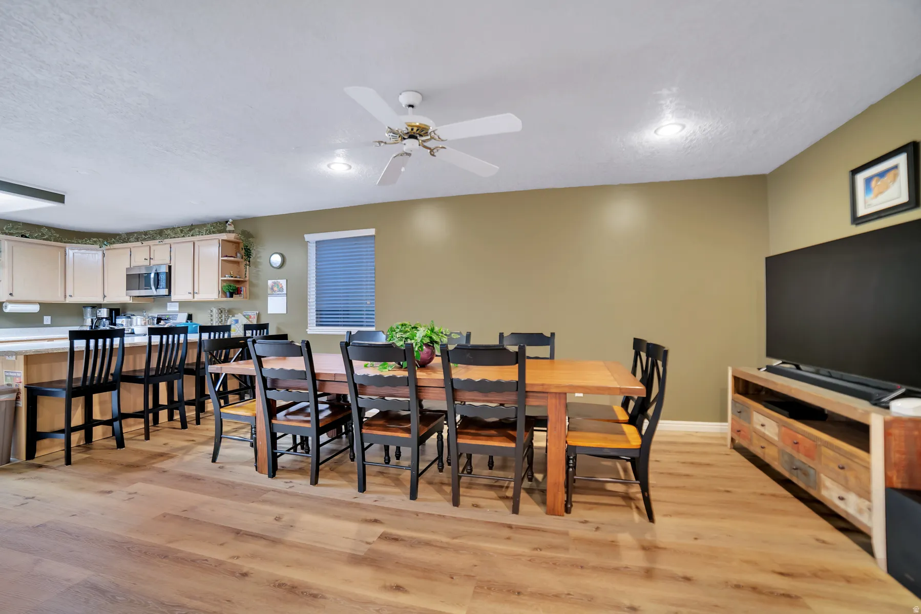 Wood-finish flooring throughout, recessed ceiling lighting, and a kitchen featuring wood cabinetry, stainless steel microwave, and a breakfast bar