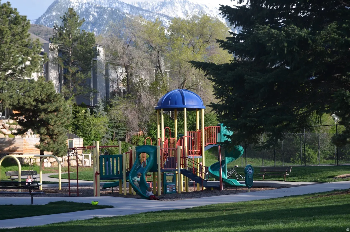 Playground featuring multiple slides, climbing structures, and swings, set on a grassy expanse with mature trees
