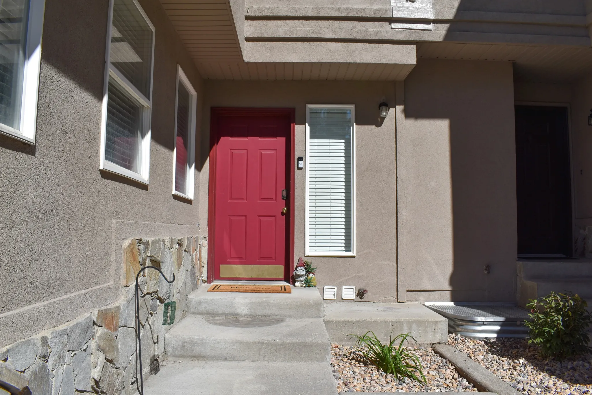 Stucco exterior with stone veneer accents, concrete steps, a prominent red entry door, and a low-maintenance gravel landscaping bed