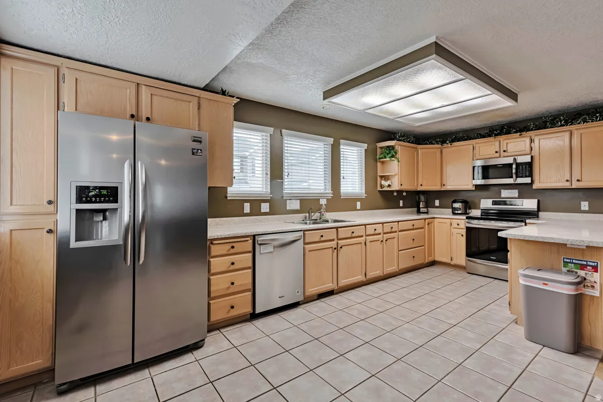 Kitchen featuring light wood cabinetry, white countertops, tile flooring, stainless steel appliances, and multiple windows
