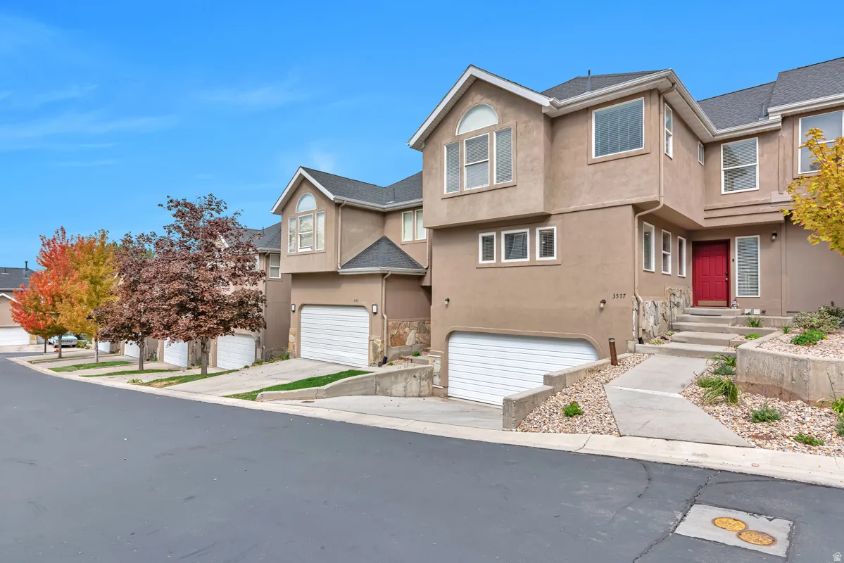 Stucco exterior with stone accents, a prominent red entry door, multiple large windows, and an attached garage with a white door