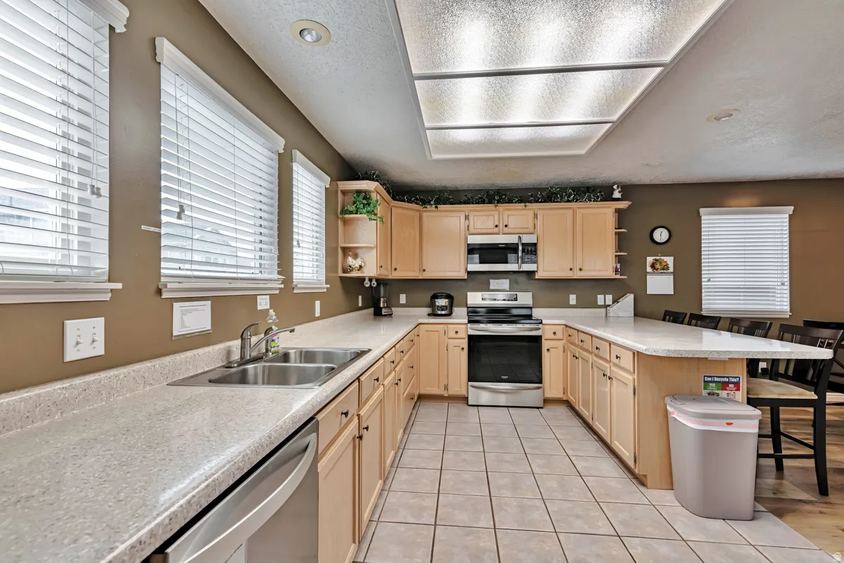 U-shaped kitchen with light wood-finish cabinetry, light-toned countertops, and a double basin stainless steel sink