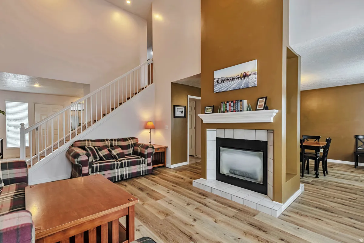 Hardwood-look flooring, two-story ceiling, white staircase with balusters, fireplace with tile surround and mantel, recessed lighting