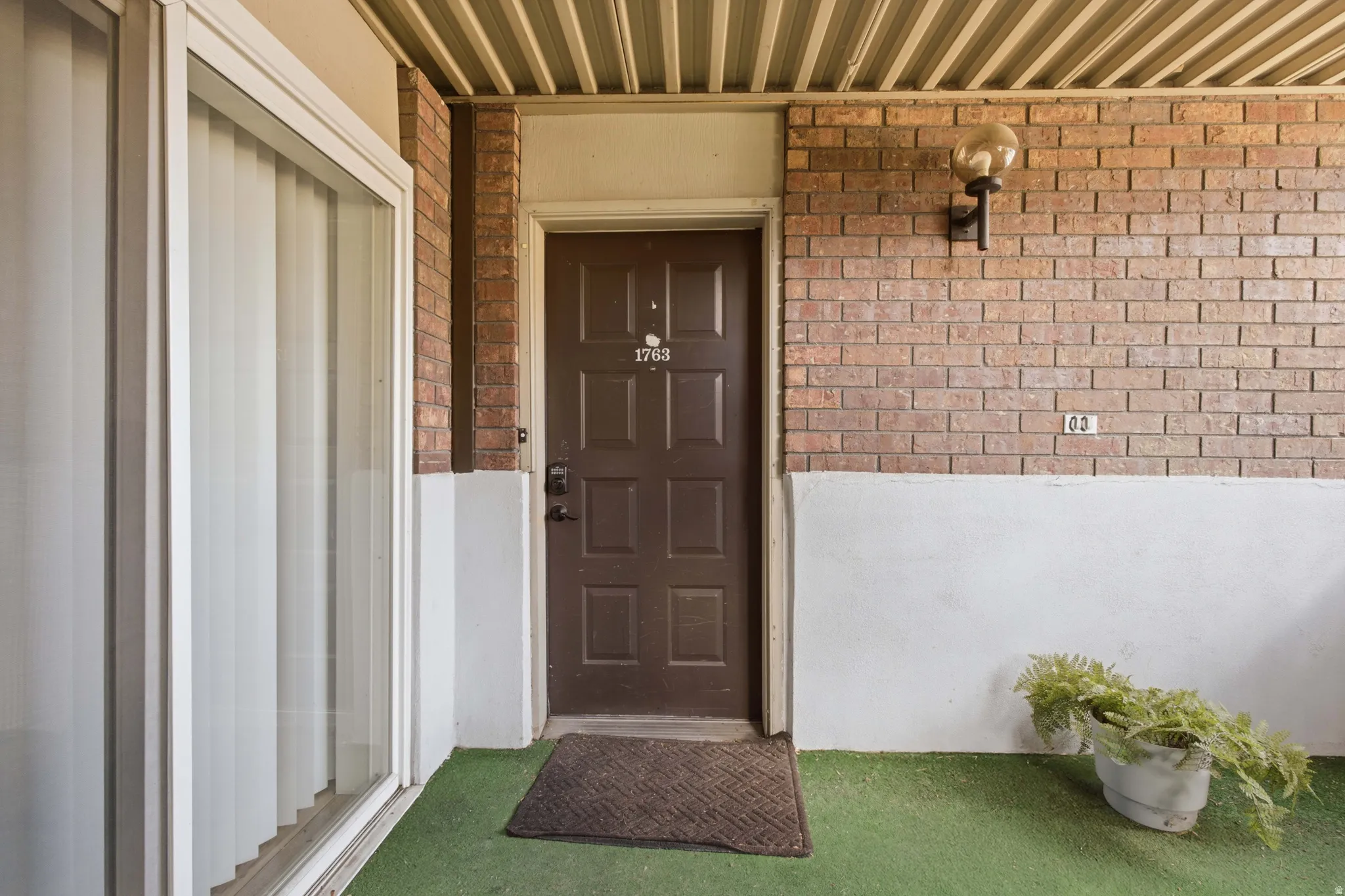 Brick exterior wall with an attached spherical light fixture, a paneled entry door, and a sliding glass door with vertical blinds
