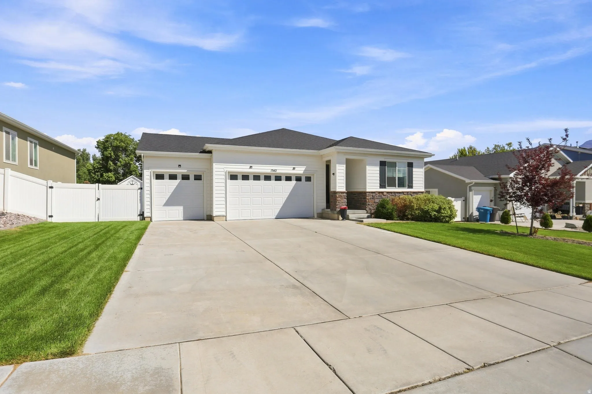 Single-story residence featuring a two-car garage, concrete driveway, and a white vinyl fence