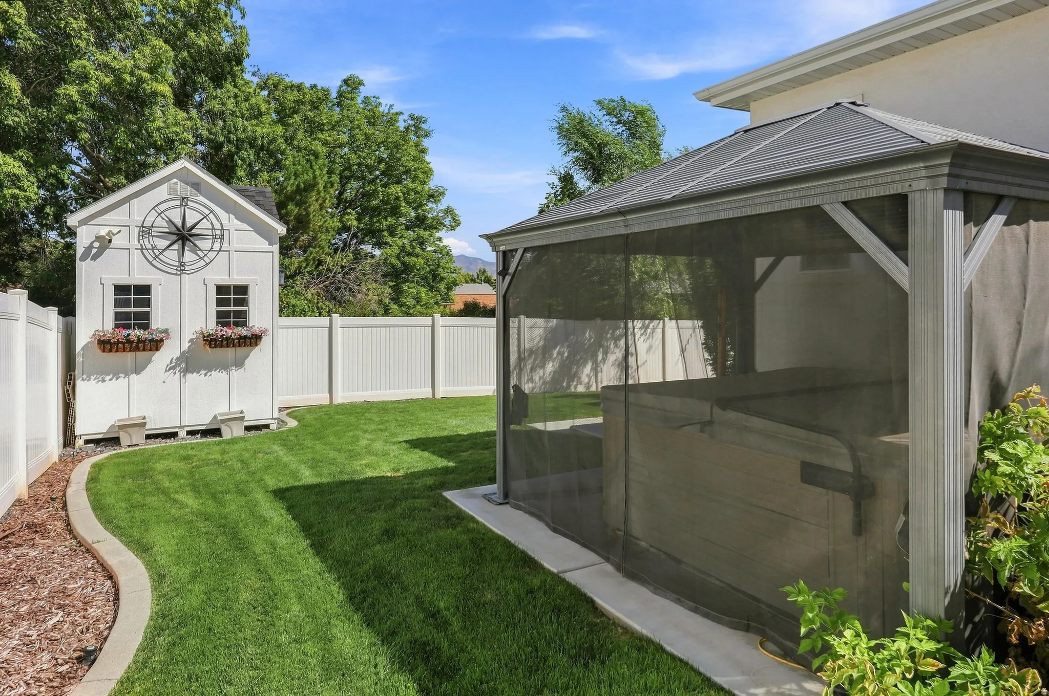 Expansive backyard featuring a hot tub enclosure, white privacy fencing, and a white storage shed