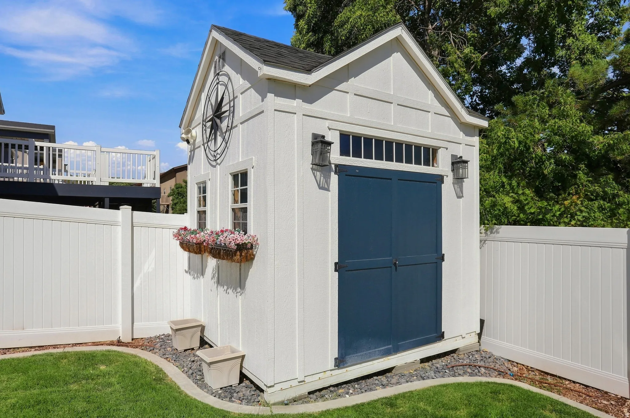 Detached shed with board and batten siding, dark blue double doors, two exterior light fixtures, and a white privacy fence