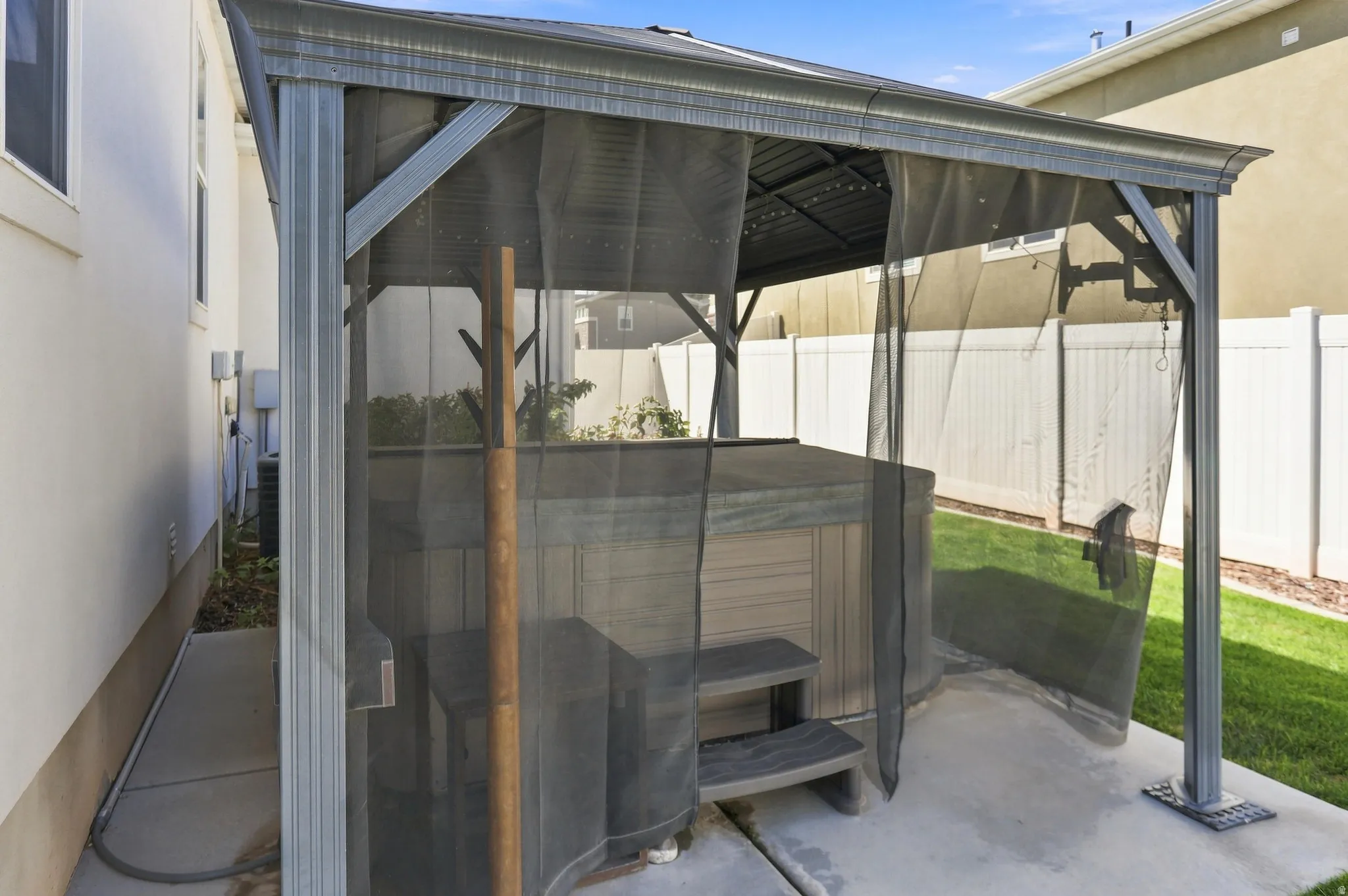 Outdoor hot tub with a protective cover, enclosed by a screened gazebo featuring a metal frame and roof