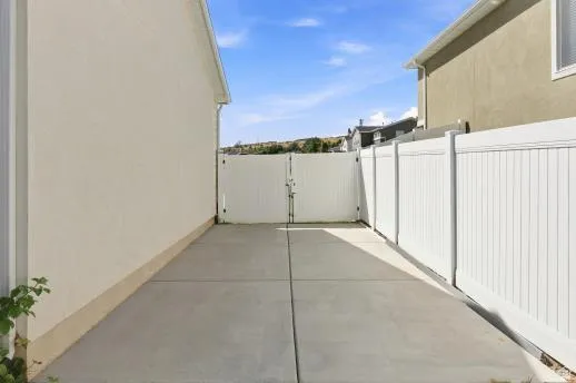 Concrete pad extending the length of the property, providing access to a white paneled privacy fence and double gate