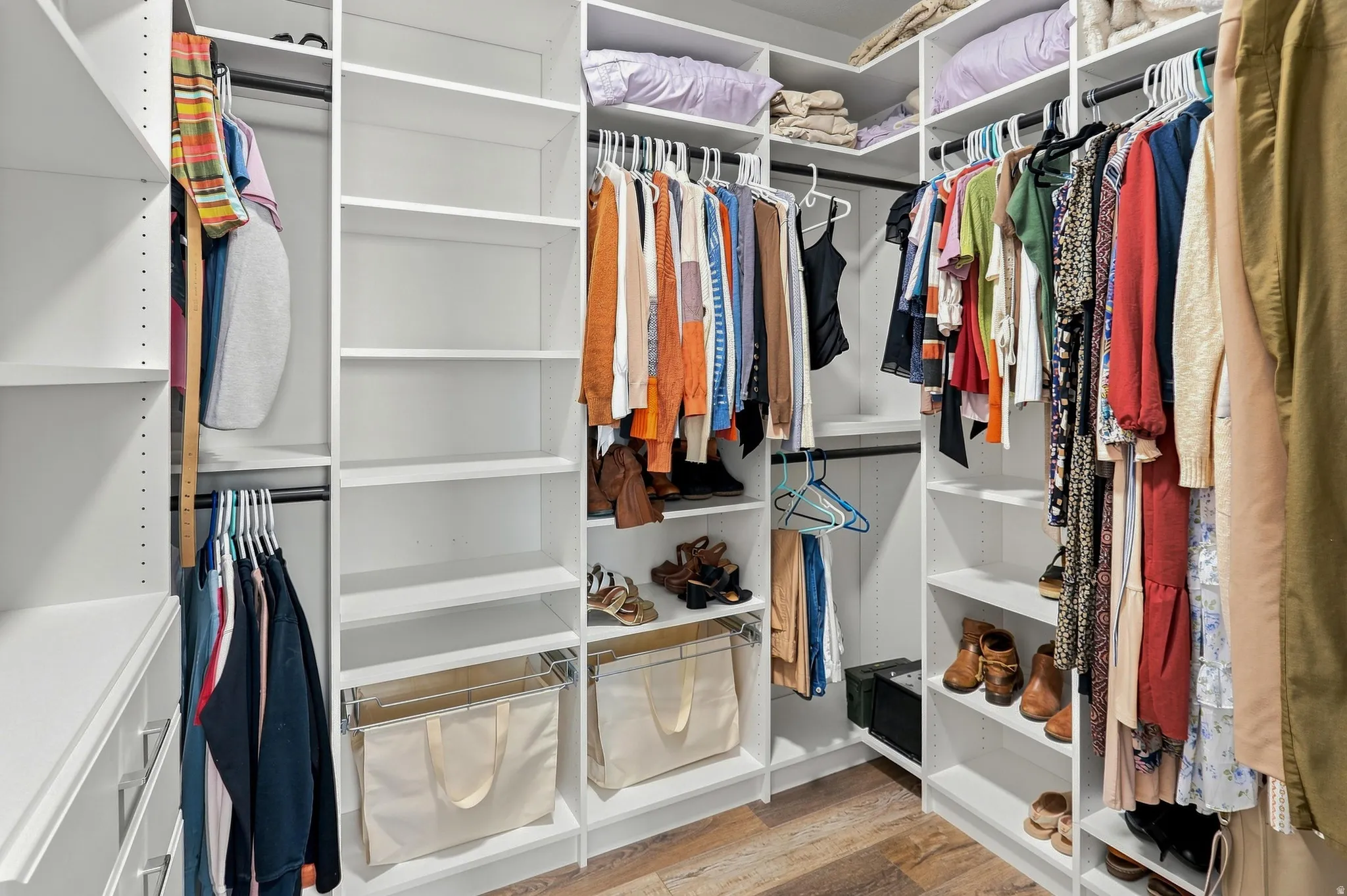 Custom closet system featuring white shelving, multiple hanging rods, and wood-finish flooring