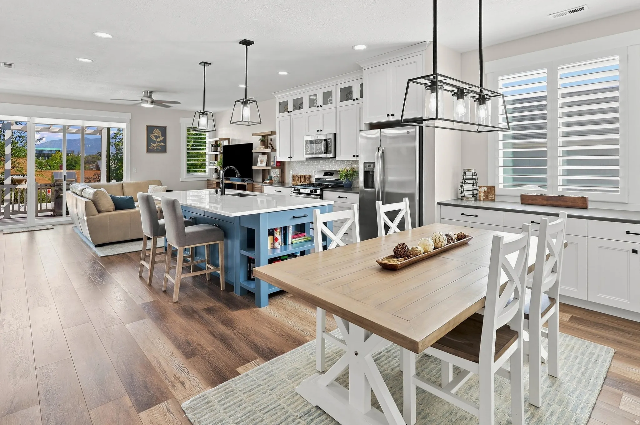 Open-concept living area with wood-finish flooring, a kitchen island with seating, white cabinetry, stainless steel appliances, and a sliding glass door