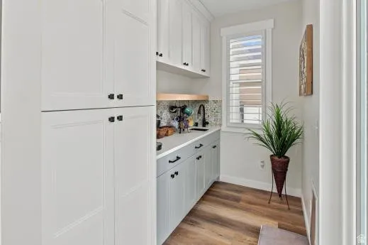 Integrated cabinetry with shaker-style doors, wood-finish flooring, undermount sink with a black faucet, and a patterned tile backsplash