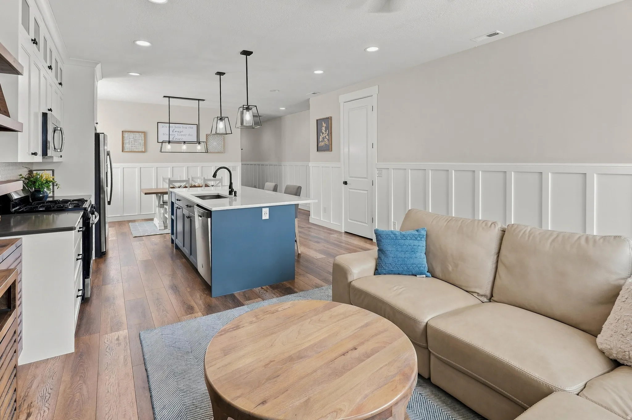 Open-concept living area featuring wood-finish flooring, a kitchen island with seating, pendant lighting fixtures, a gas range, and wainscoting