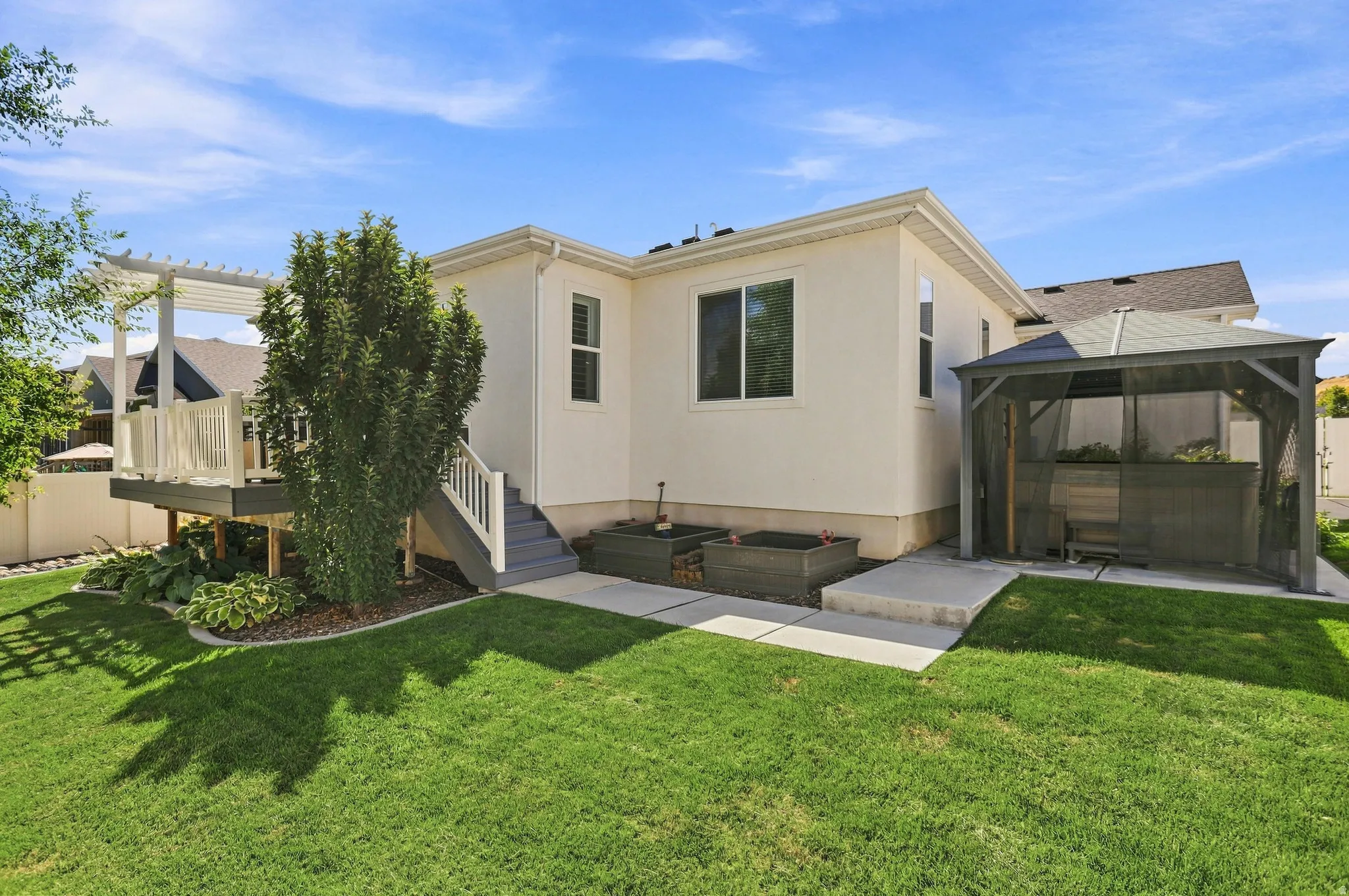 Expansive green lawn, elevated deck with pergola, exterior staircase, concrete patio, and raised planters