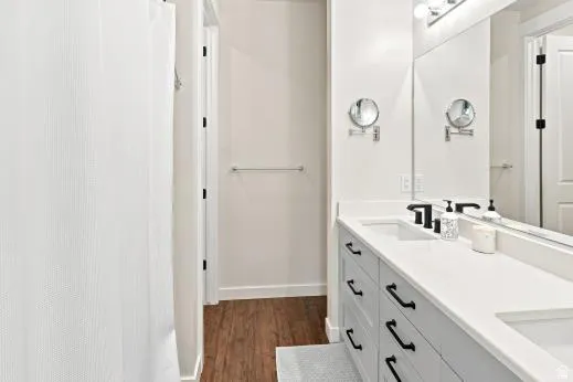 Dual vanity with white countertops, integrated sinks, black fixtures, and wood-finish flooring