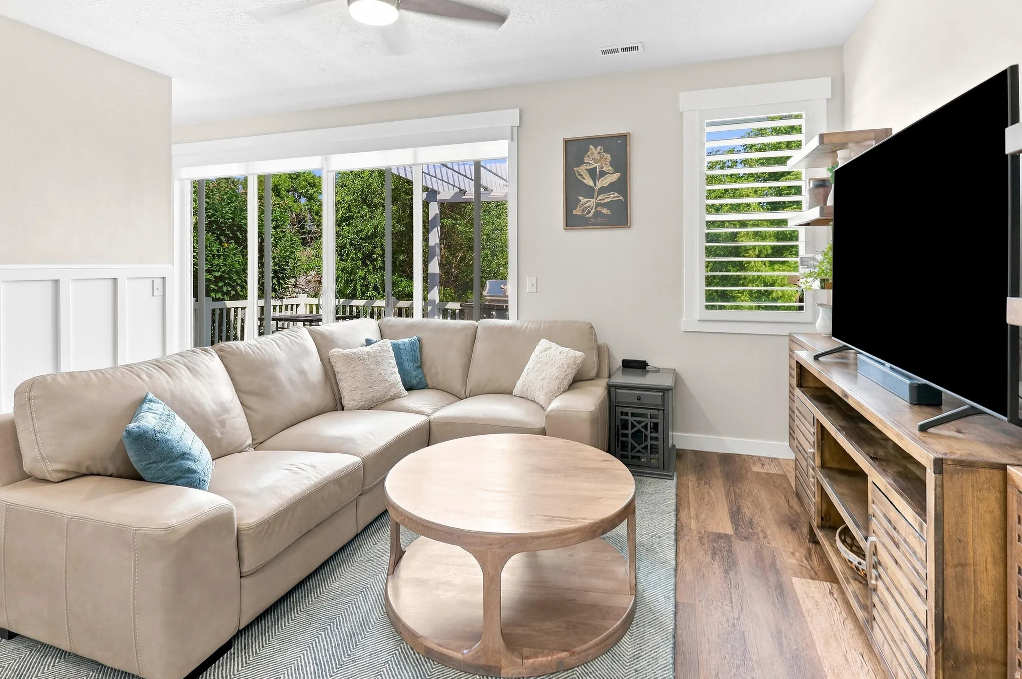 Wood-finish flooring, white paneled wall accents, sliding glass door, white window trim, and a ceiling fan