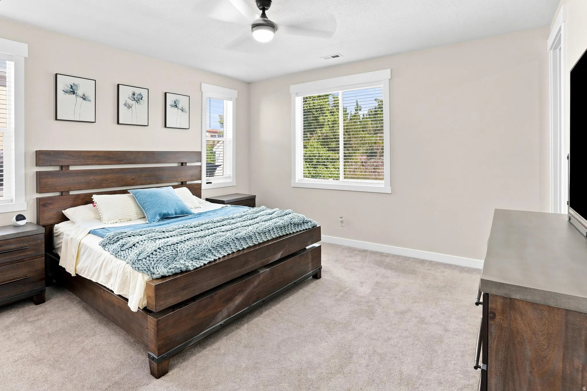 Plush carpeted flooring, multiple windows with blinds, a ceiling fan with integrated lighting, and neutral wall tones