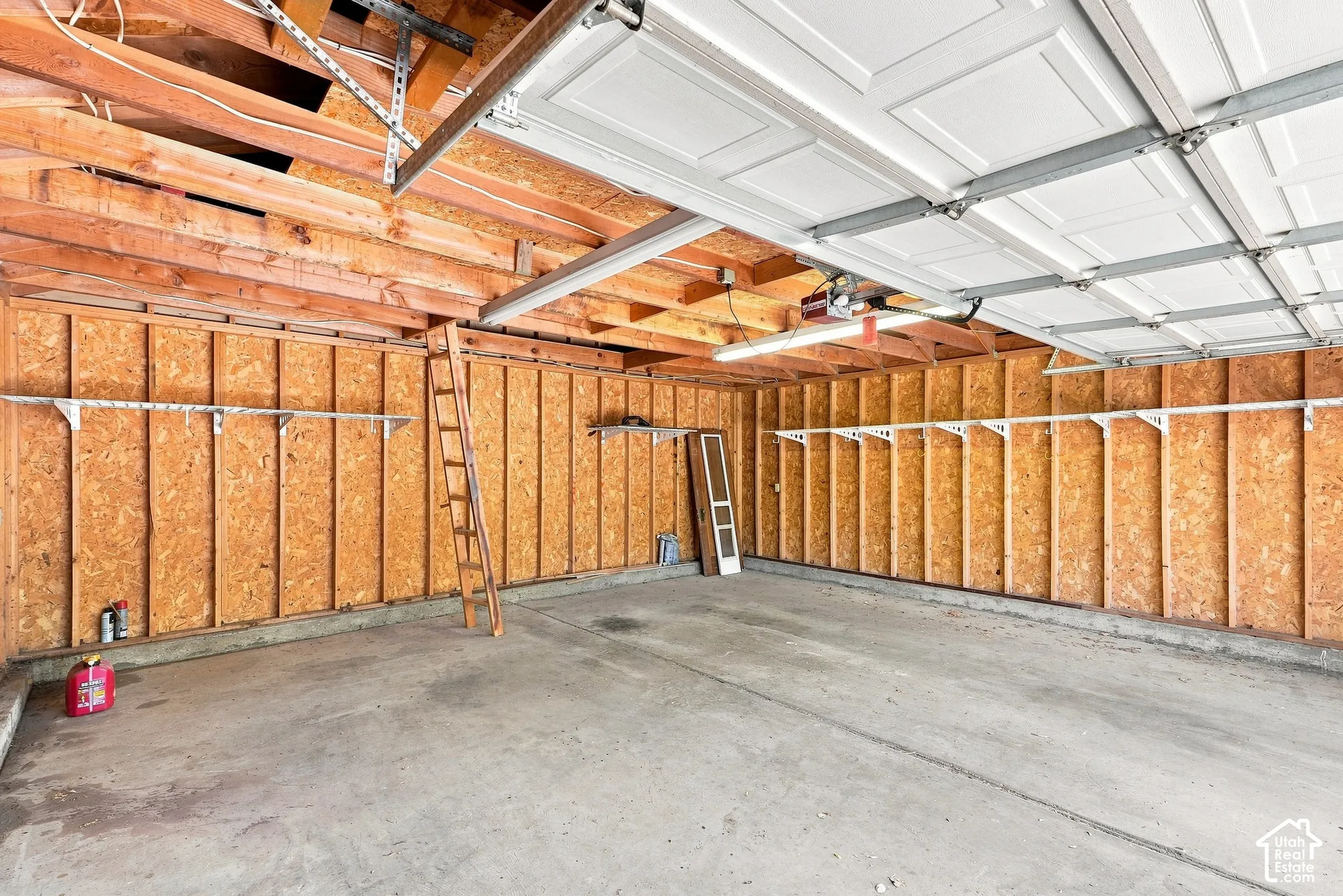 Spacious garage interior with exposed wood-beam ceiling, recessed lighting, concrete flooring, and fiberglass insulation throughout walls