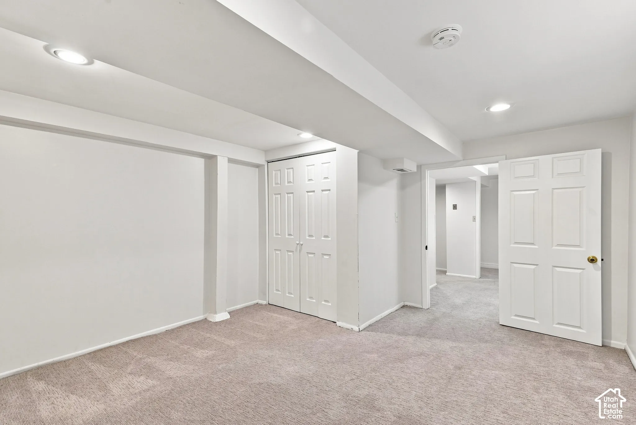 Spacious finished basement featuring neutral carpet flooring, recessed ceiling lighting, multiple white six-panel closet doors, and an open floor plan with structural support columns