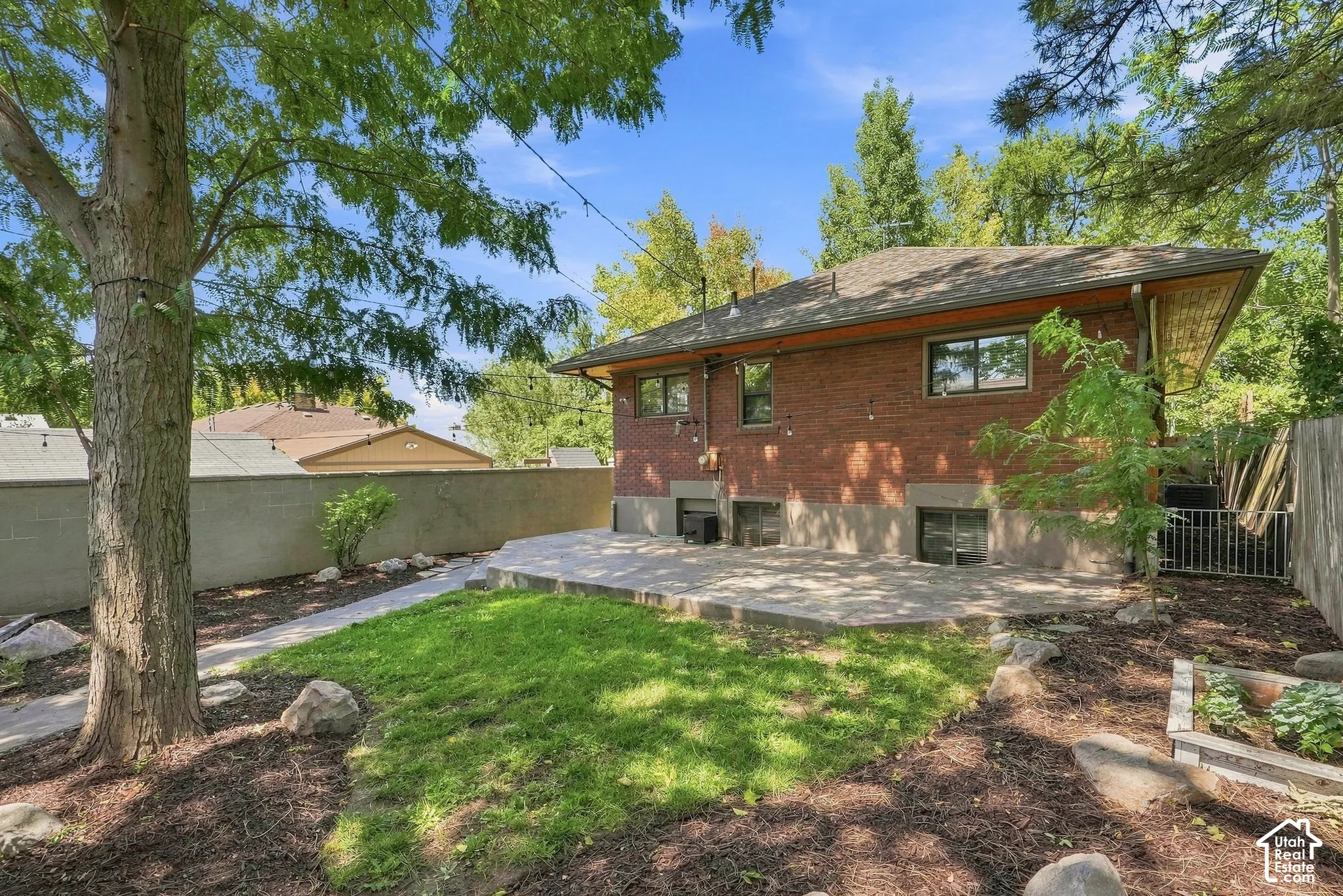 Brick Colonial residence with a spacious backyard featuring mature shade trees, a manicured lawn, mulched landscaping beds, and a rear patio area