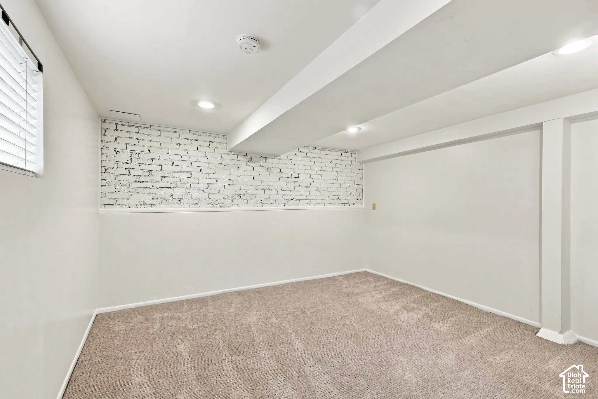 Finished basement featuring neutral wall finishes, recessed ceiling lighting, carpeted flooring, and an accent brick wall detail