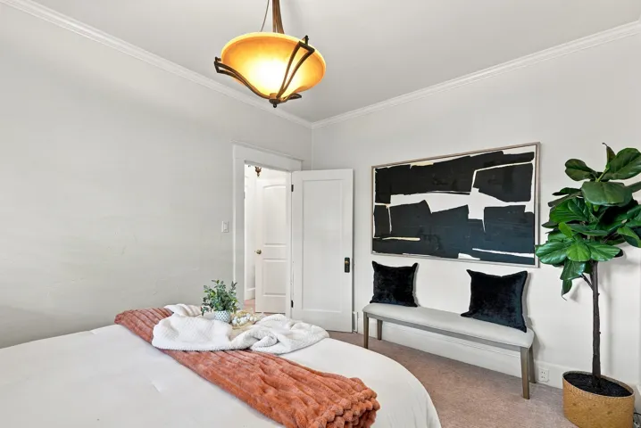 Bright bedroom with soft-close closet doors, recessed ceiling lighting with brass pendant fixture, and potted greenery