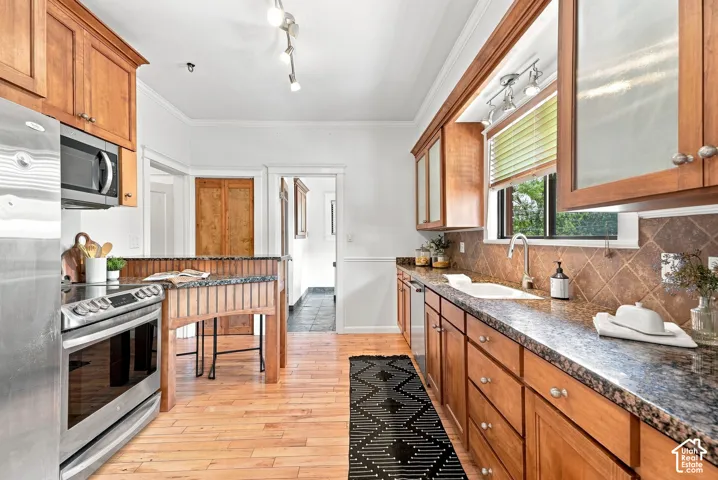 Galley kitchen featuring warm wood cabinetry, stainless steel appliances, wood-finish flooring, granite countertops, and a tile backsplash