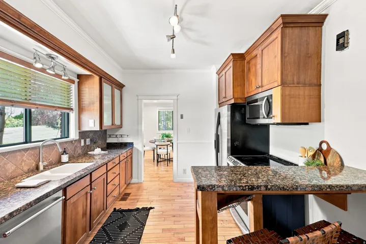 Galley kitchen with warm wood cabinetry, granite countertops, and stainless steel appliances including a built-in microwave