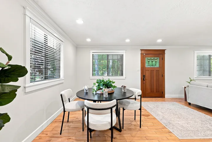 Bright dining area featuring a round black table with wood-finish flooring, recessed ceiling lighting, and multiple windows with plantation shutters