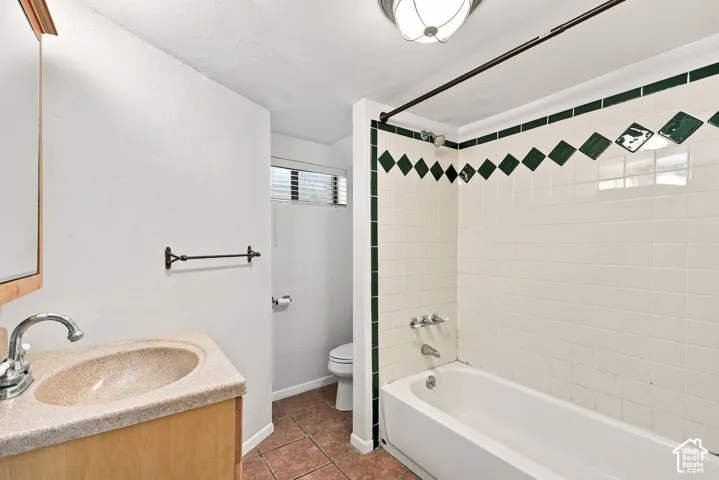 Ceramic tile flooring, vanity with integrated sink, white subway tile shower surround with green accent tiles, and a built-in bathtub