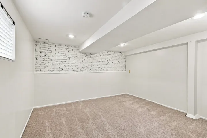 Finished basement featuring neutral wall finishes, recessed ceiling lighting, carpeted flooring, and an accent brick wall detail