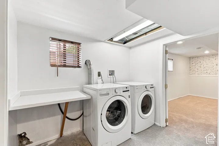 Modern laundry room featuring side-by-side front-load washing machines, white cabinetry with countertop workspace, skylights providing natural illumination, and neutral concrete flooring