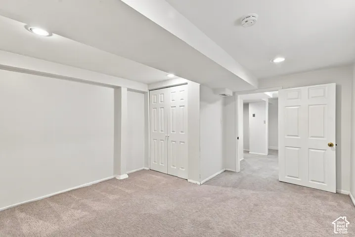 Spacious finished basement featuring neutral carpet flooring, recessed ceiling lighting, multiple white six-panel closet doors, and an open floor plan with structural support columns
