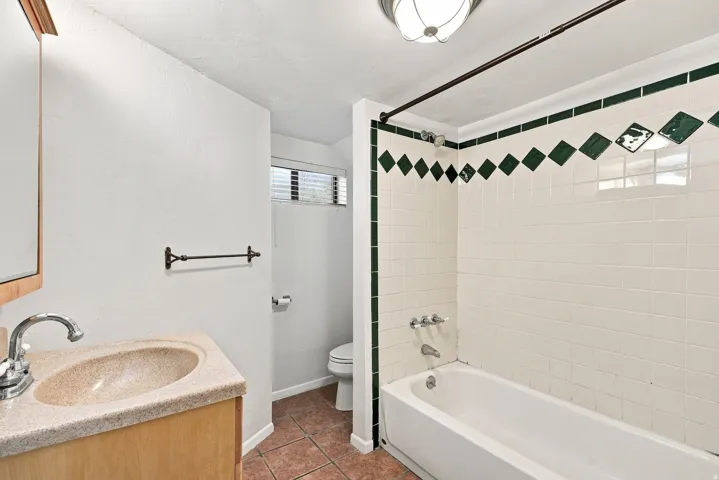 Ceramic tile flooring, vanity with integrated sink, white subway tile shower surround with green accent tiles, and a built-in bathtub