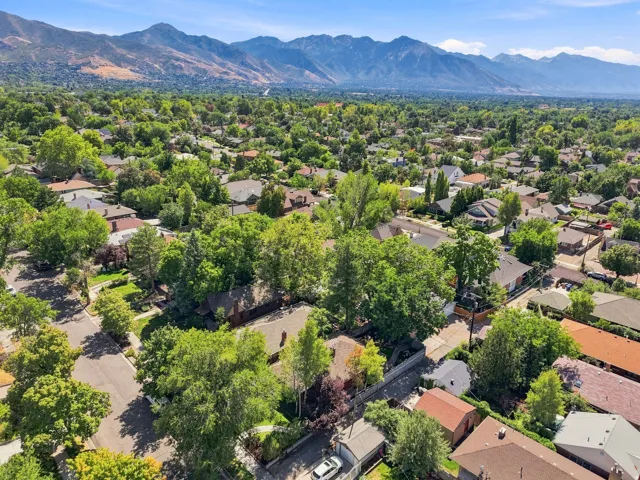 Aerial view showcasing a tree-lined residential neighborhood with mature landscaping, situated against a dramatic mountain backdrop