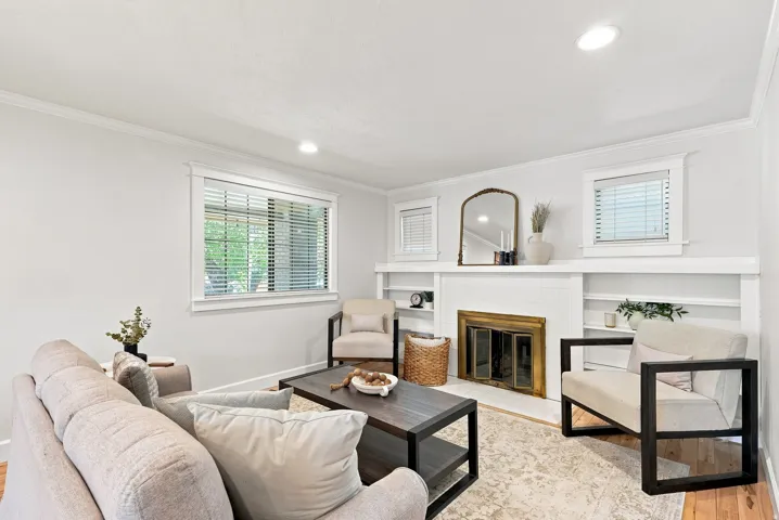 Recessed lighting, crown molding, white fireplace with brass-finish doors, built-in shelving, and wood-finish flooring