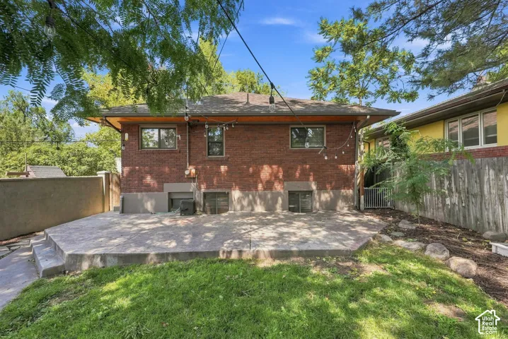 Brick exterior with a concrete patio, wood fencing, and mature trees