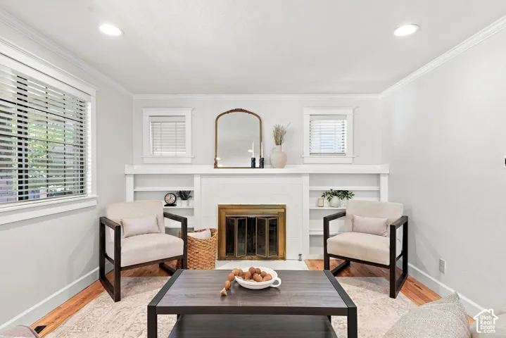 Recessed ceiling lighting, wood-finish flooring, white crown molding, and a fireplace with integrated shelving