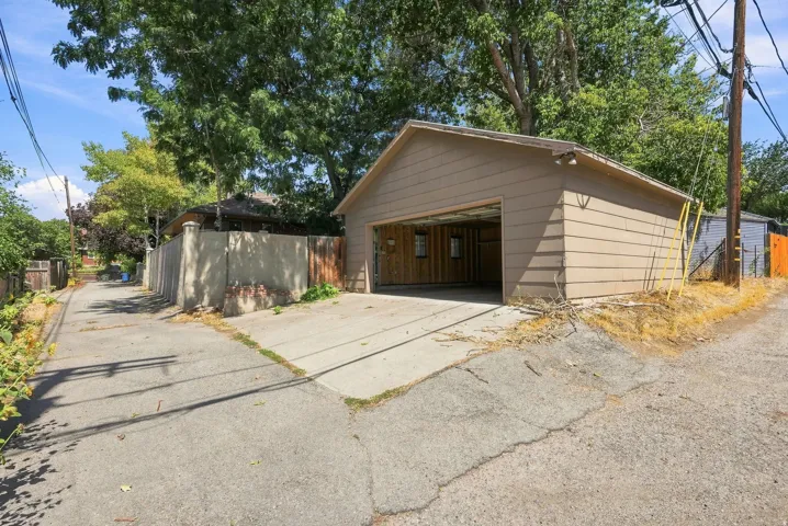 Detached garage with overhead door and concrete driveway, situated on a tree-lined lot with mature landscaping and wooden perimeter fencing