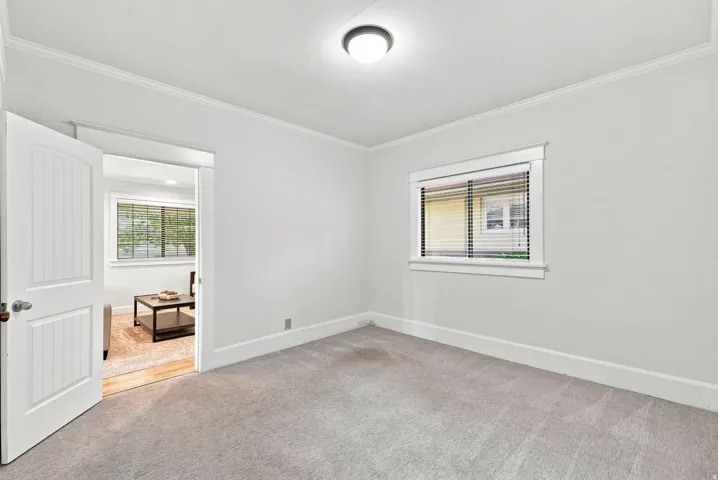 Bright secondary bedroom featuring neutral carpeting, generous natural light from dual windows, and clean white wall finishes with crown molding detail