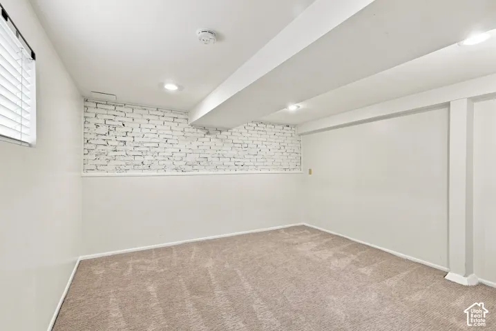Finished basement featuring neutral wall finishes, recessed ceiling lighting, carpeted flooring, and an accent brick wall detail